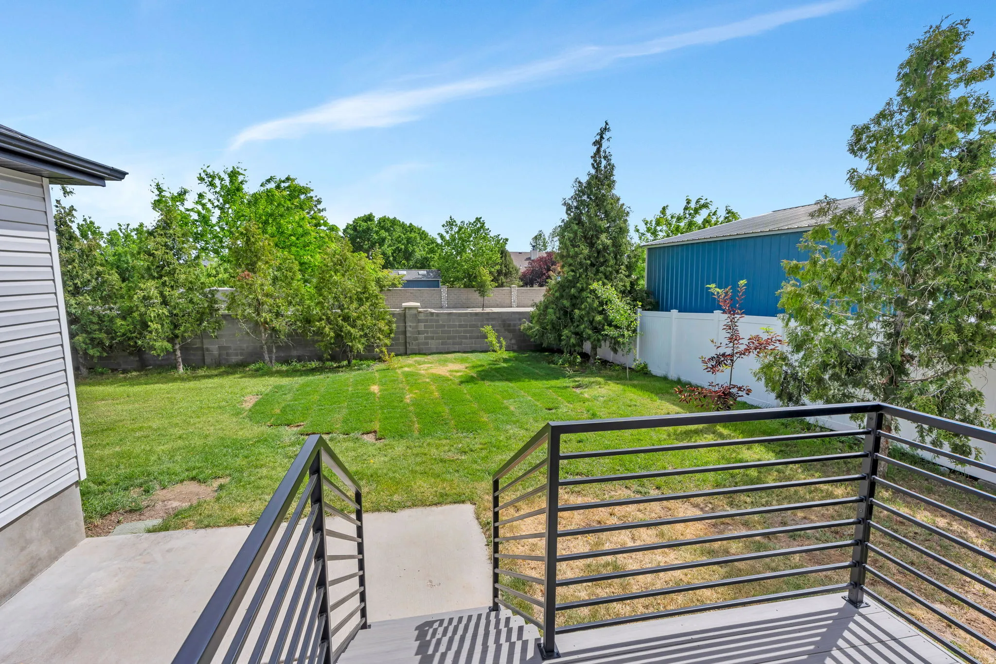 Expansive backyard featuring a manicured lawn, established trees, and concrete block retaining wall