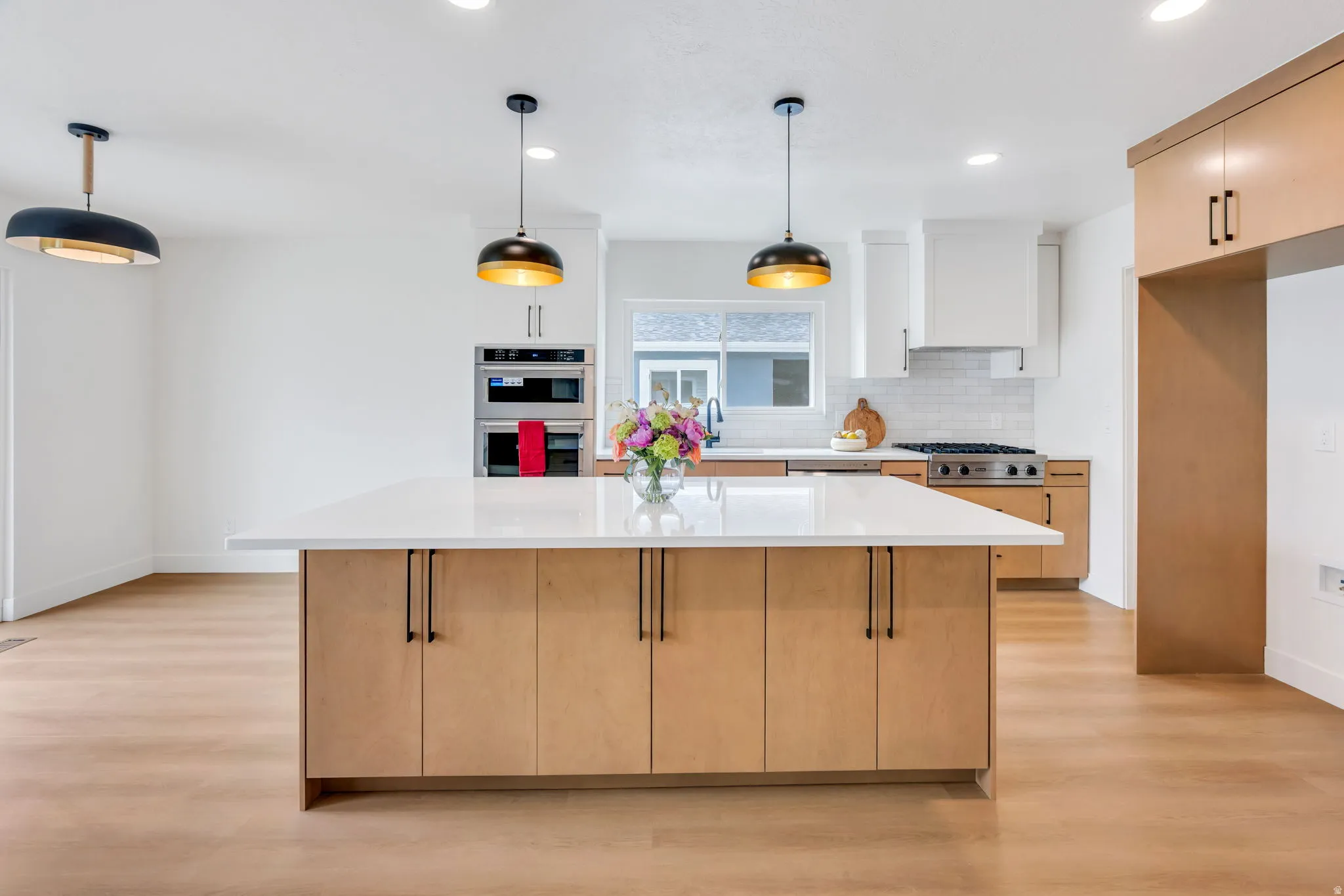 Open-concept kitchen featuring a large island with a light-toned countertop, stainless steel appliances, wood-finish flooring, recessed lighting, and modern pendant fixtures