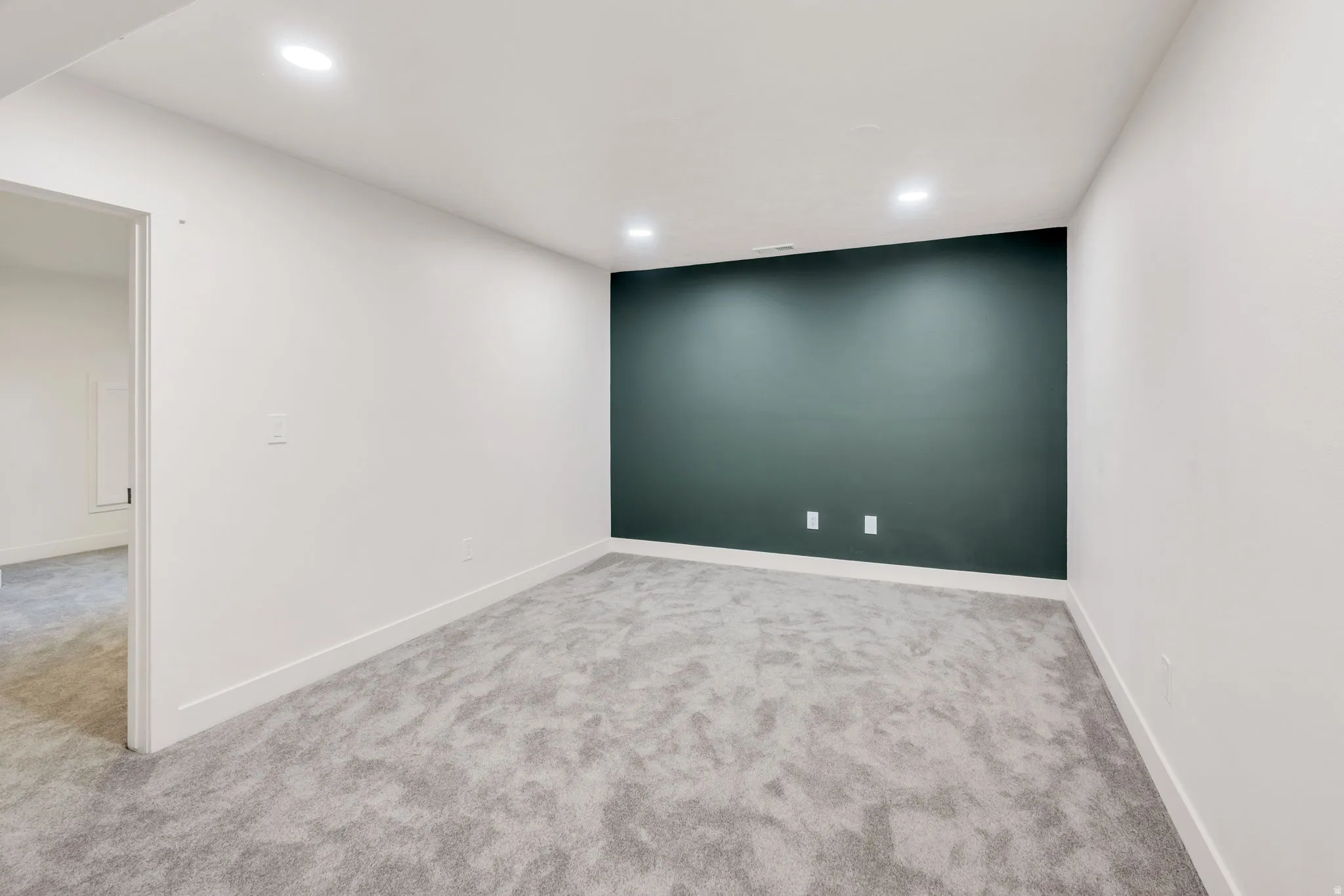 Spacious room featuring a dark accent wall, recessed lighting, light gray carpeting, and white baseboards
