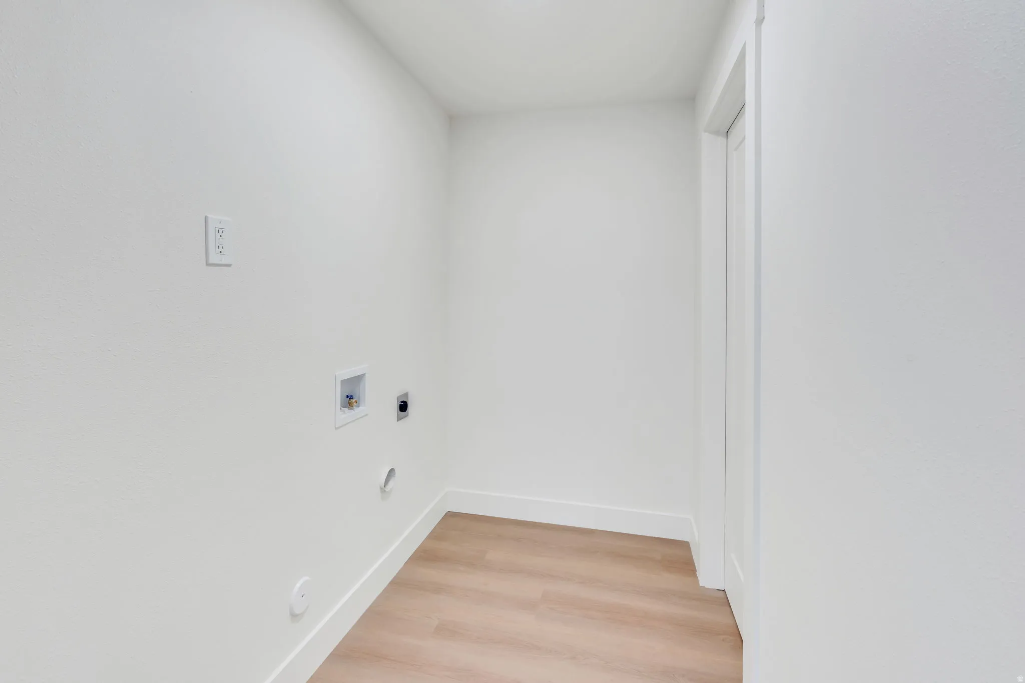 Dedicated laundry space featuring wood-finish flooring, white walls, and a door frame