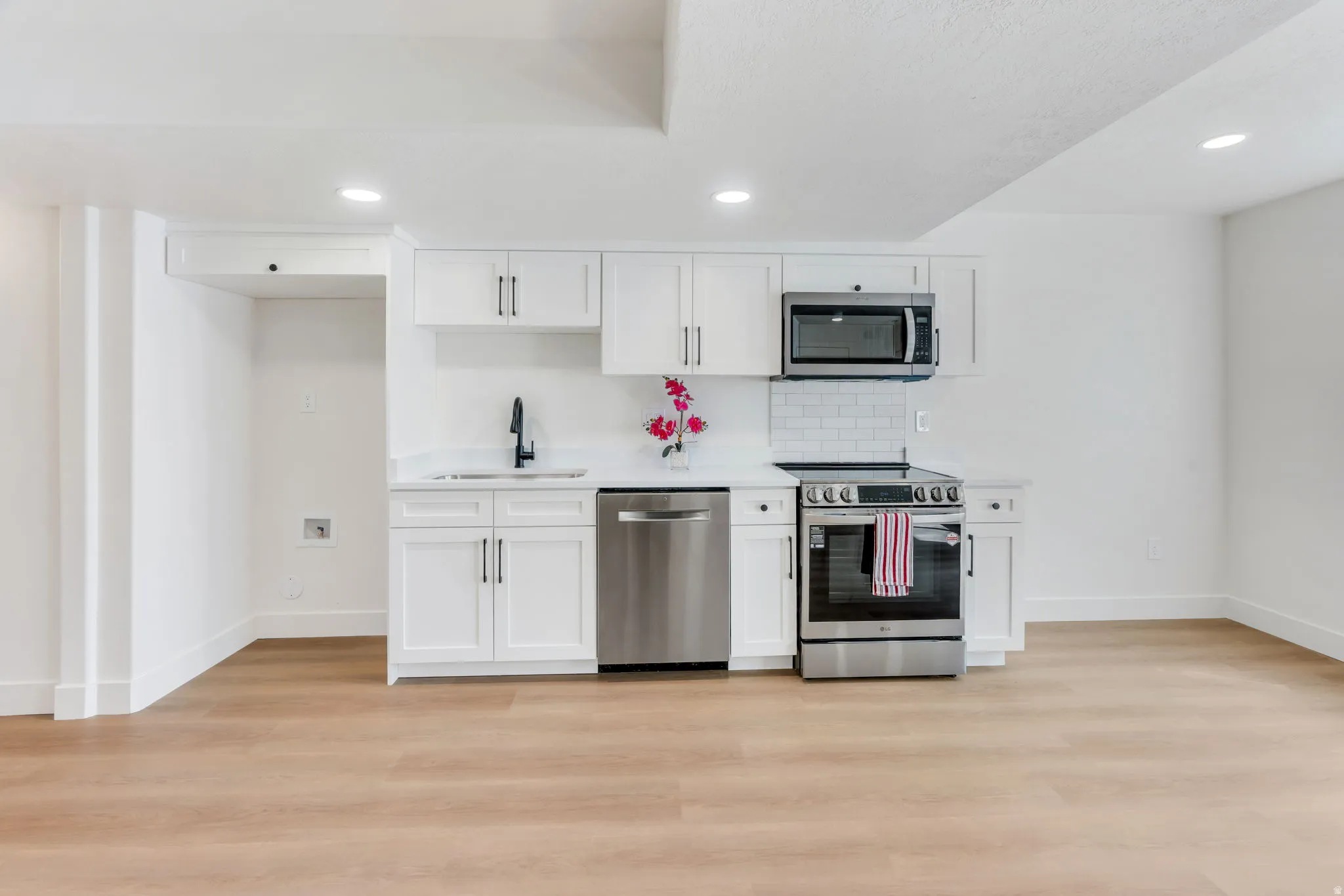 Compact kitchen featuring white shaker cabinetry, stainless steel appliances, a subway tile backsplash, and light wood-finish flooring