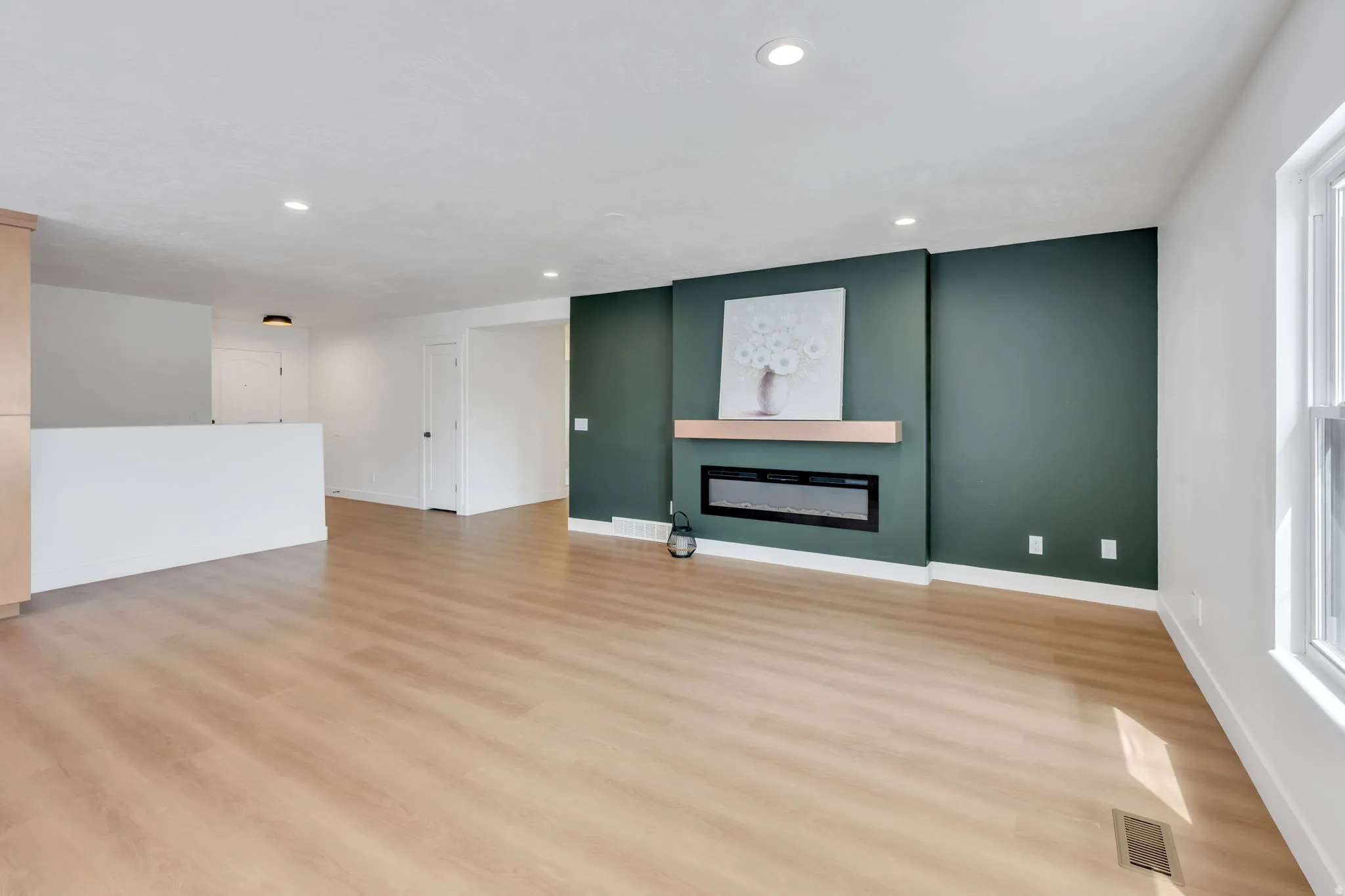 Spacious room featuring wood-finish flooring, recessed lighting, and a prominent feature wall in a deep green hue
