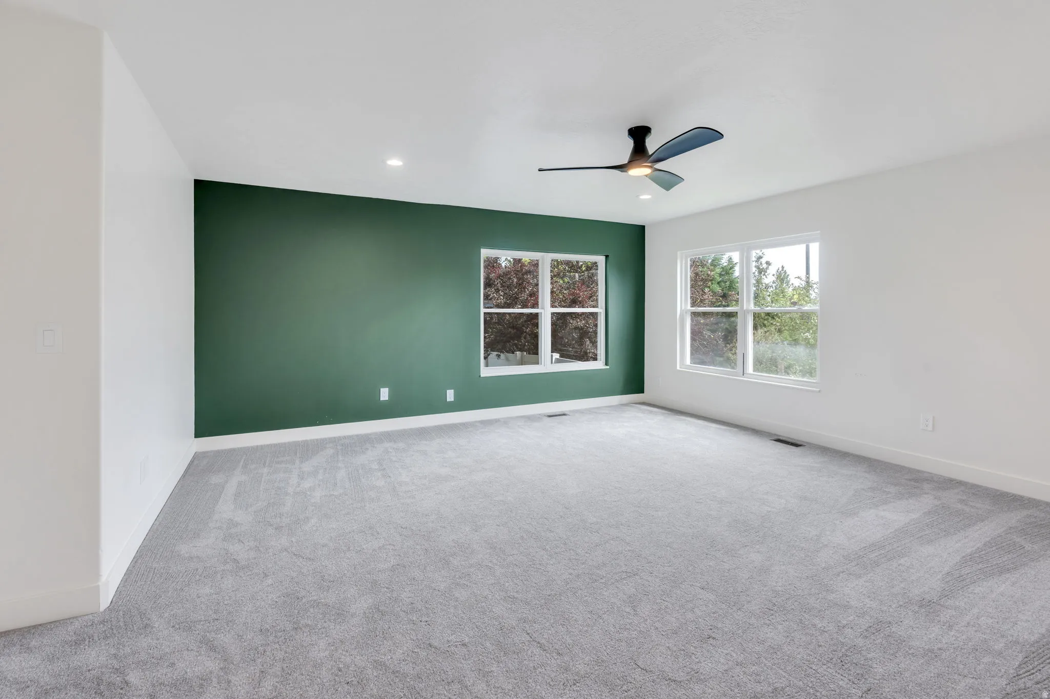 Spacious room featuring a deep green accent wall, light grey carpeting, recessed lighting, and multiple windows