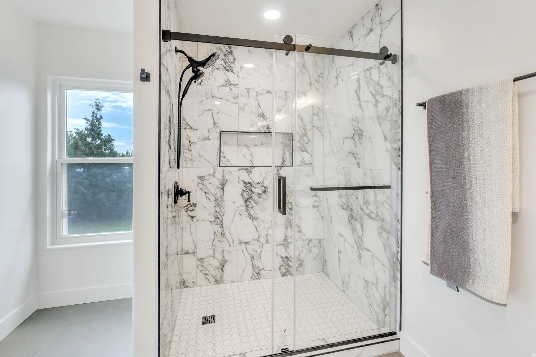 Spacious shower with marble-look tile surround, hexagon tile flooring, and matte black fixtures