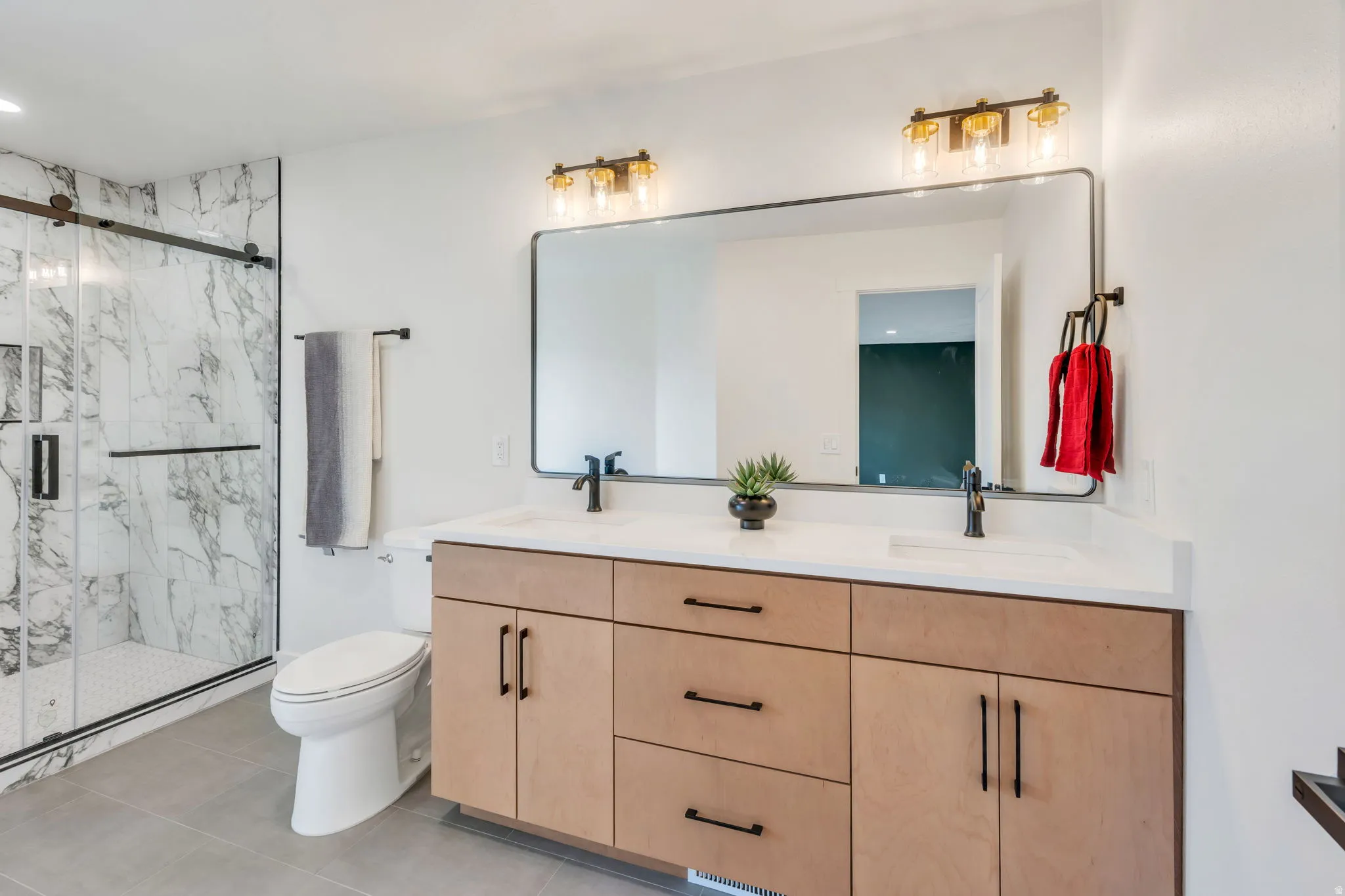 Spacious bathroom featuring a dual vanity with light wood-finish cabinetry, quartz countertops, and matte black fixtures