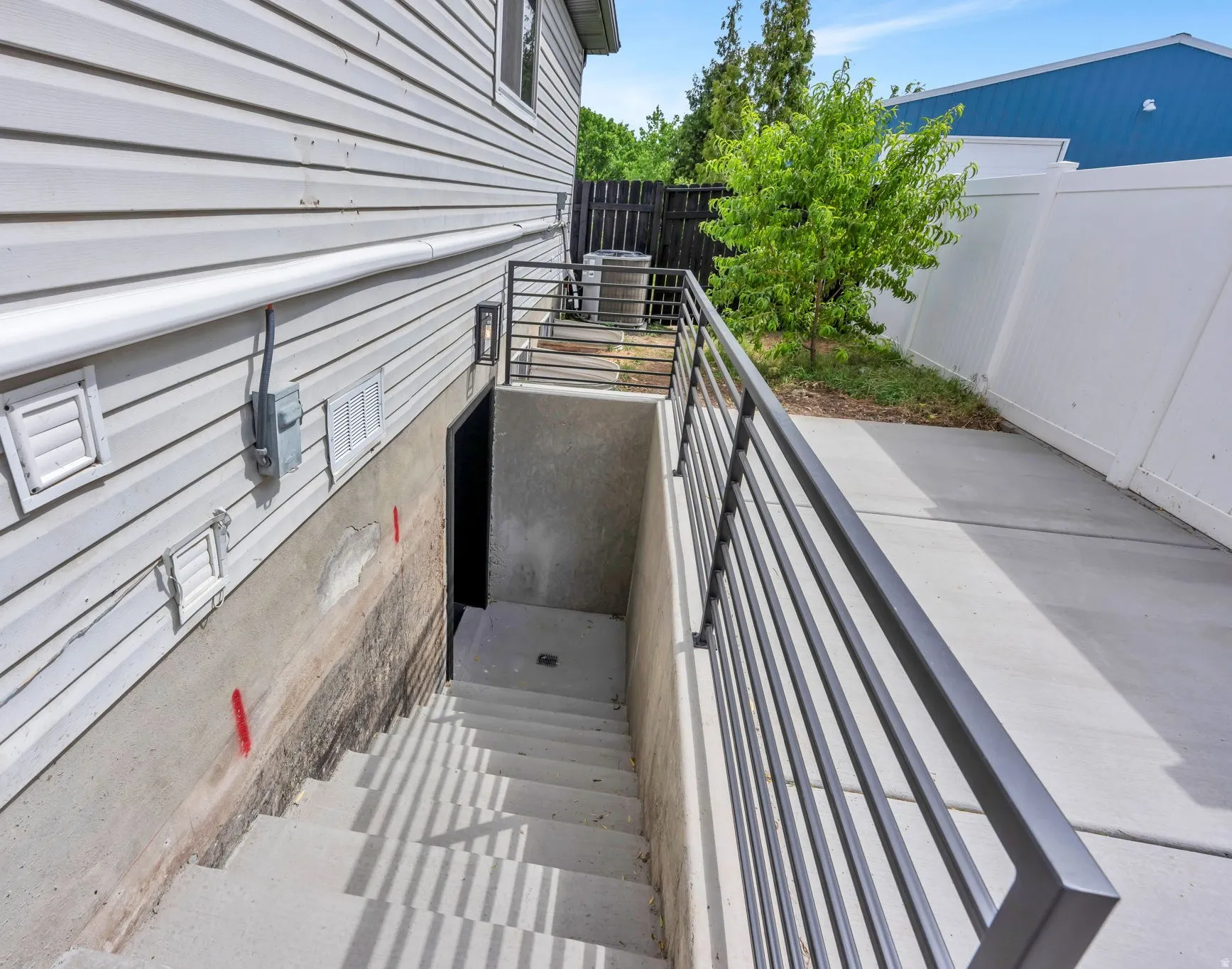 Concrete basement stairwell with modern horizontal metal railings, leading to an exterior basement entry