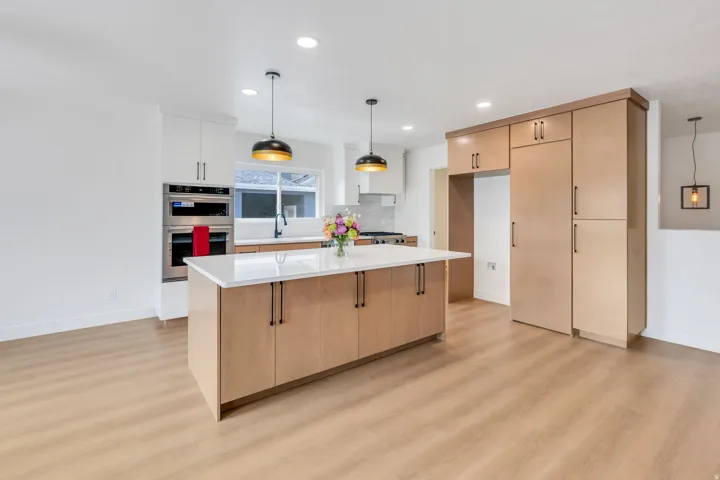Kitchen featuring a substantial island with a white countertop and wood-finish cabinetry, stainless steel double wall ovens, recessed lighting, and wood-finish flooring