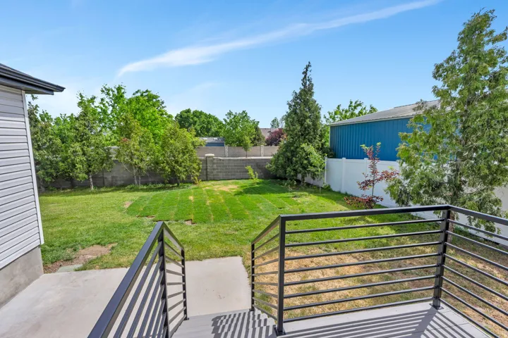 Expansive backyard featuring a manicured lawn, established trees, and concrete block retaining wall