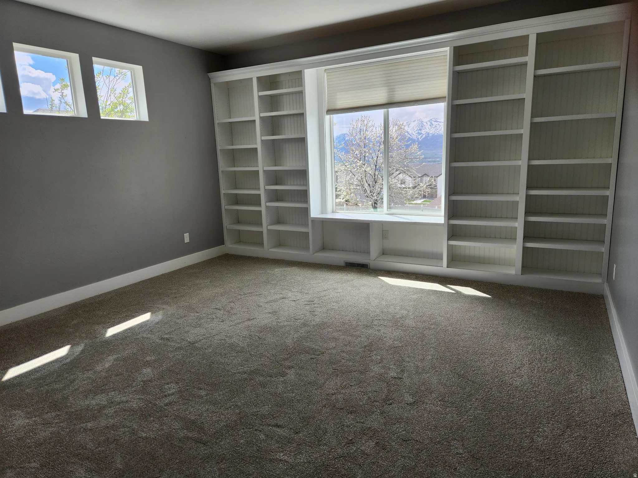 Main floor primary bedroom features custom built-in shelving and window seat framing a large picture window