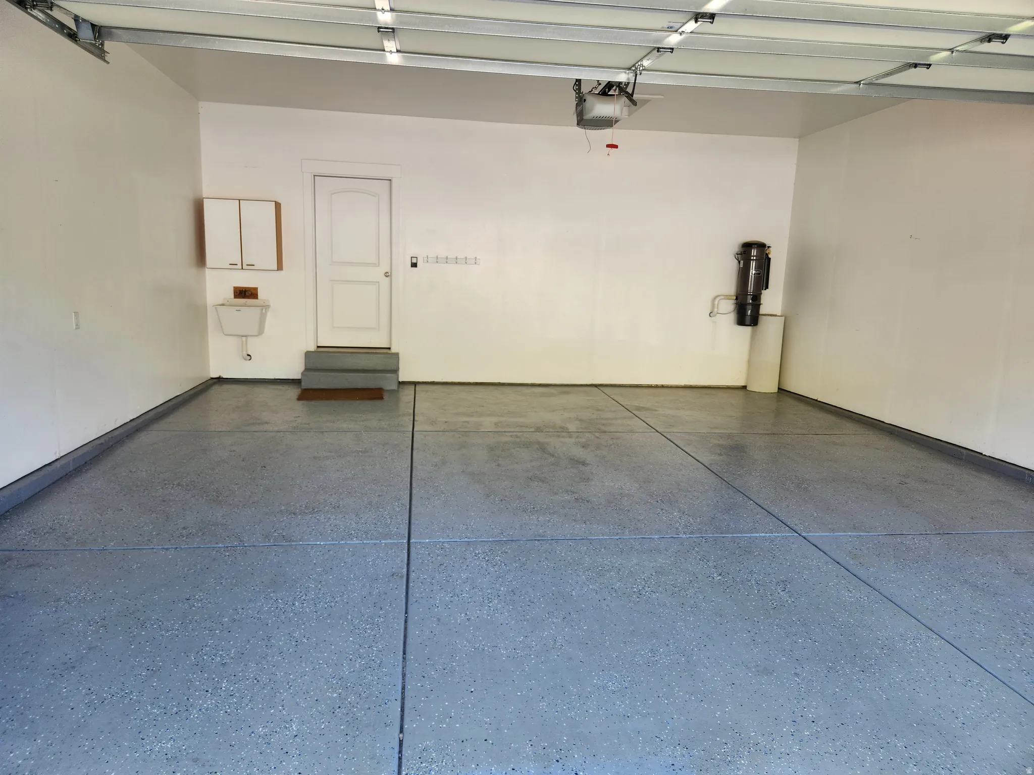 Spacious over-sized garage featuring a speckled epoxy floor, white walls, and a utility sink