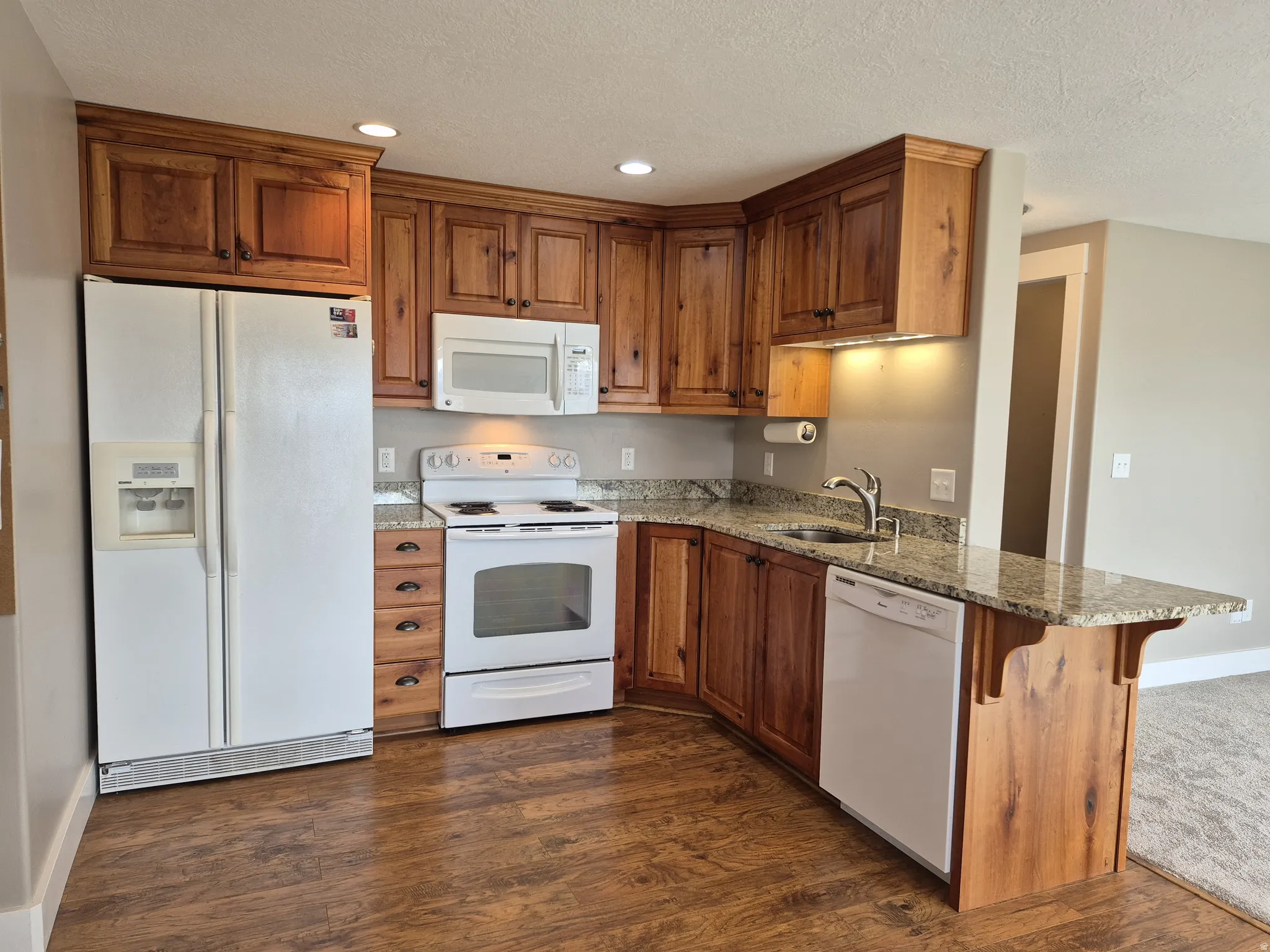 Kitchen featuring wood-finish cabinetry, granite countertops, and a full suite of white appliances