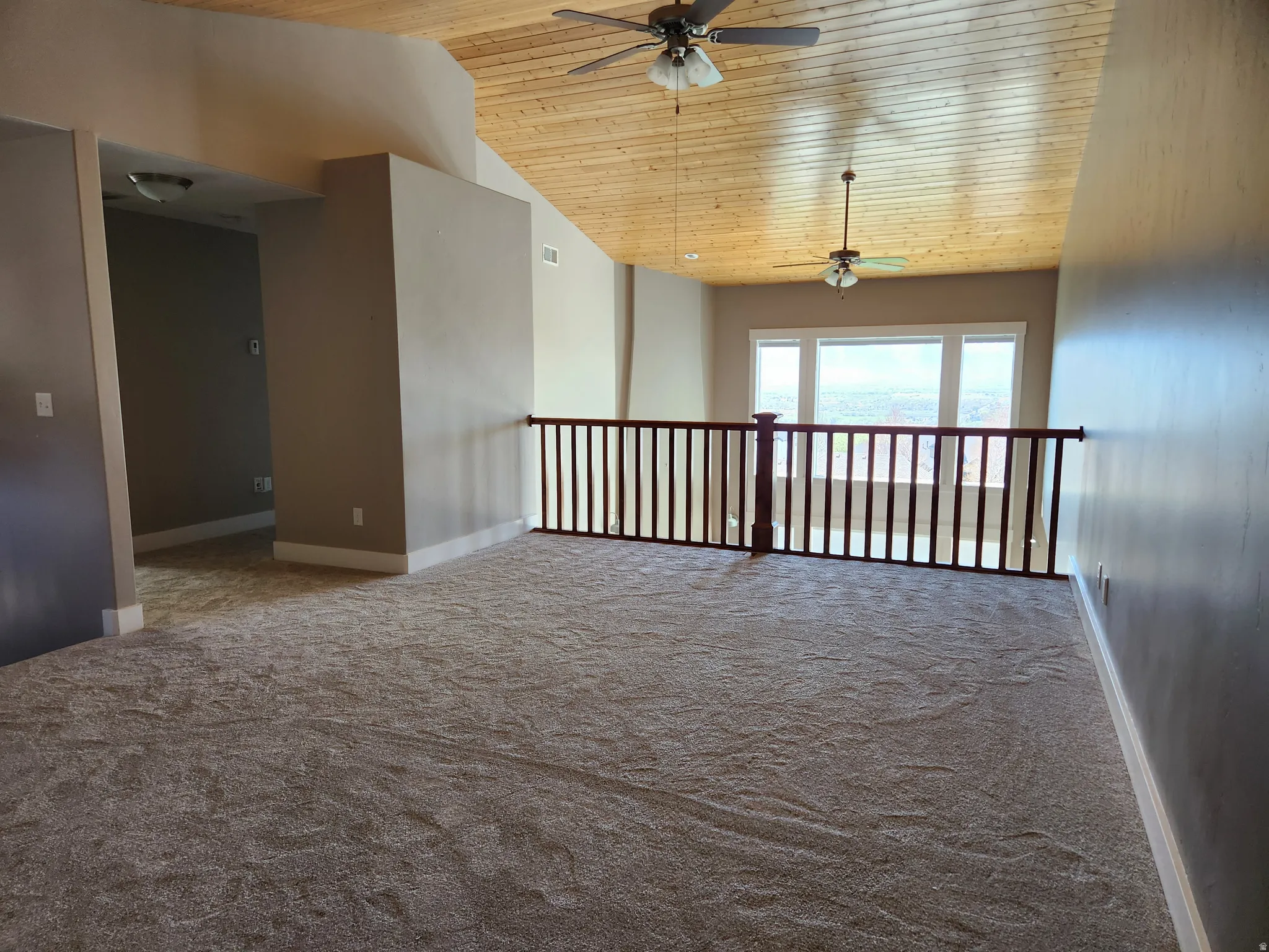 Spacious loft area featuring a vaulted wood-finish ceiling, two ceiling fans, a wood railing overlooking the lower level, and a multi-pane window.