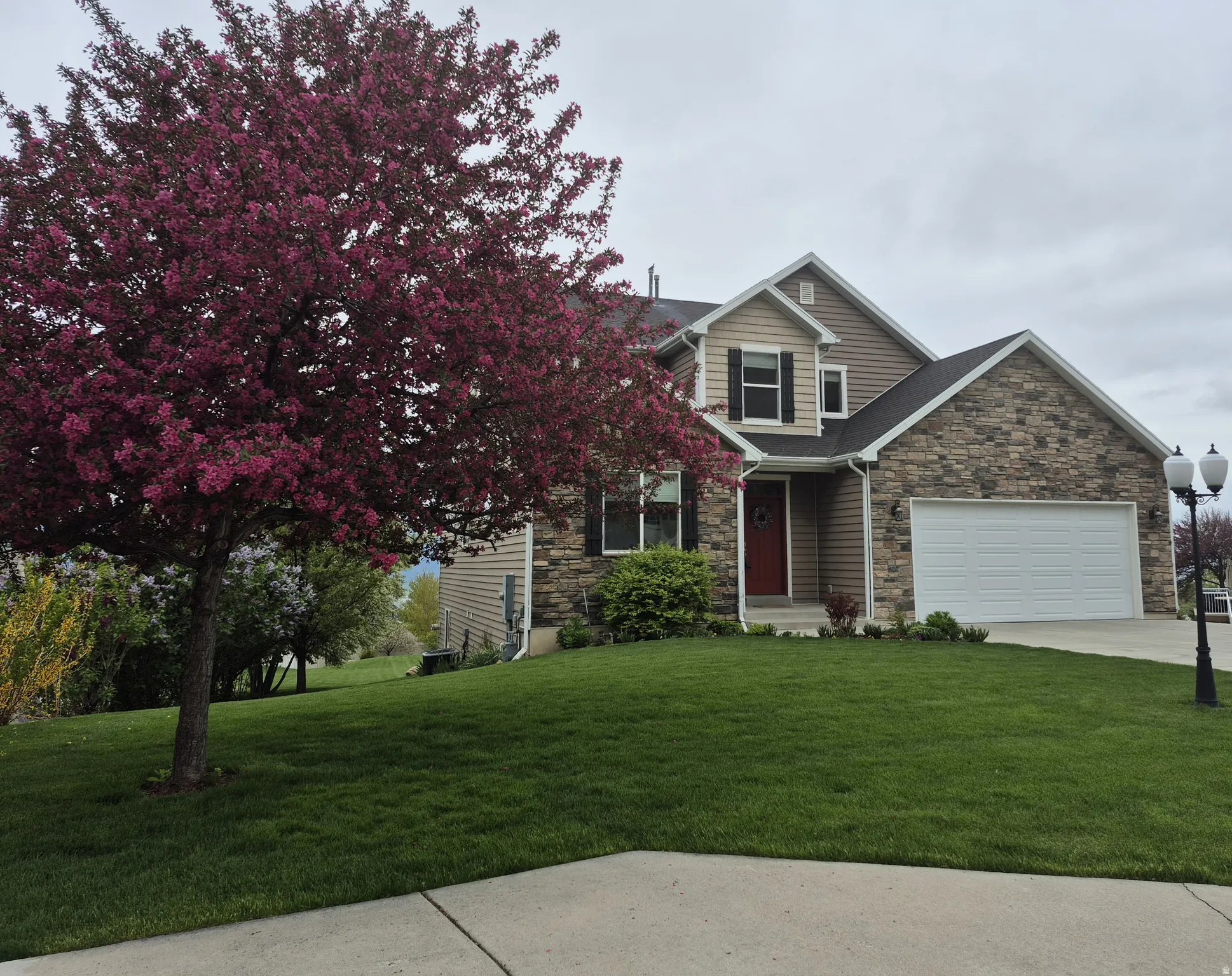 Two-story residence featuring stone and siding exterior accents, a prominent red entry door, an attached over-sized two-car garage, and a manicured front lawn