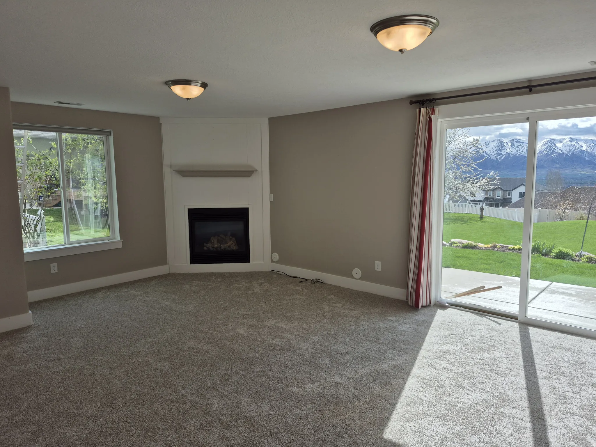 Spacious room featuring a corner fireplace with a white mantel, large windows, and neutral carpeting