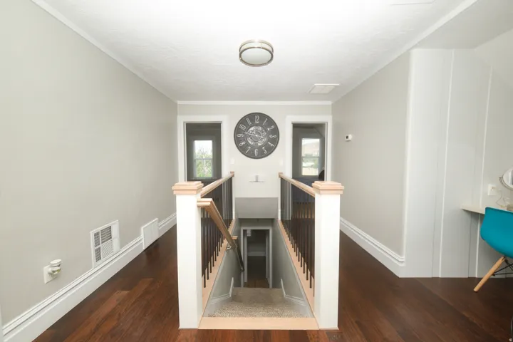 Upper-level landing featuring wood-finish flooring, a contemporary ceiling light fixture, and a staircase with light wood newel posts and dark balusters