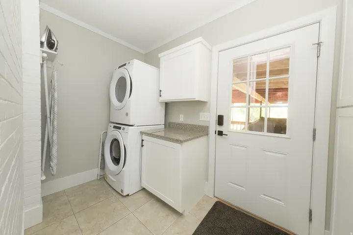 Dedicated laundry area featuring stacked appliances, built-in cabinetry, a stone-finish countertop, tiled flooring, and a glass-paned exterior door