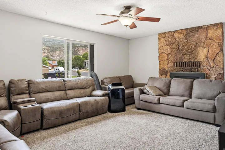 Spacious living area featuring a stone fireplace, large window, and ceiling fan with integrated lighting