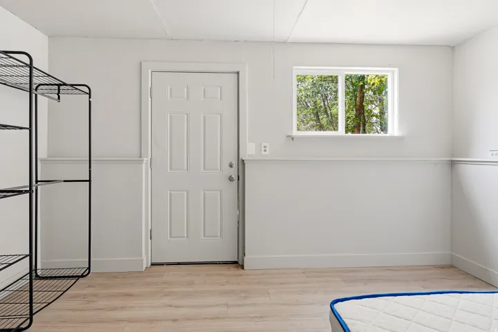 Light-toned wood-finish flooring complements the crisp white walls and trim in this room featuring a white paneled door and a dual-pane window