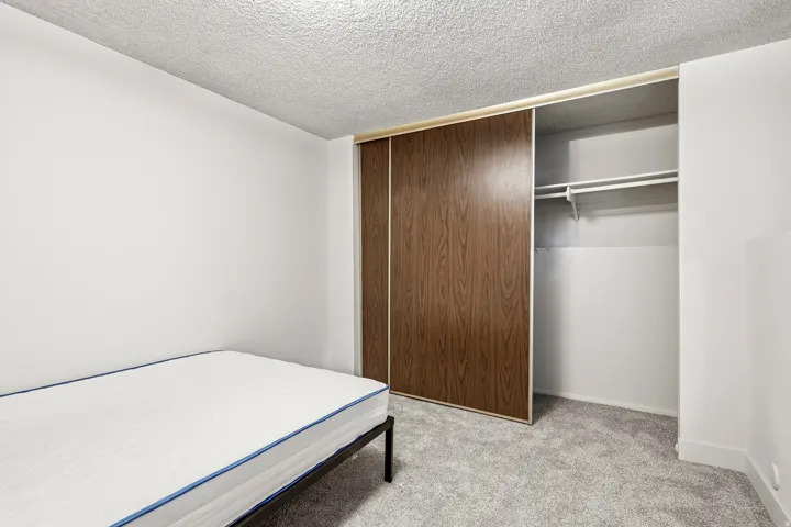 Bedroom featuring wood-finish sliding closet doors, white walls, and light gray carpet flooring