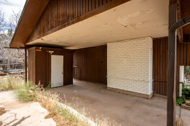Covered carport with concrete flooring, featuring vertical wood paneling and a white painted brick accent wall
