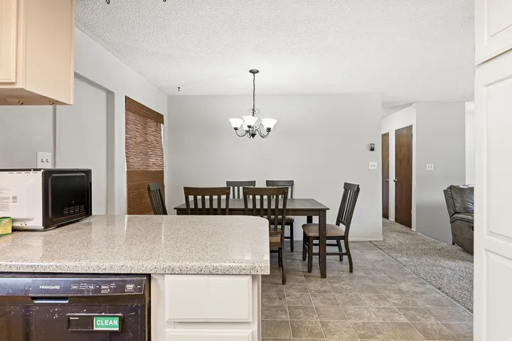 Kitchen counter with stone-finish countertop, white cabinetry, and an integrated dishwasher