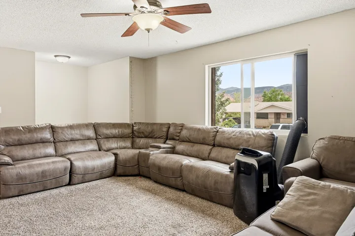 Bright living area featuring neutral-toned walls, textured carpeting, and a ceiling fan with integrated lighting