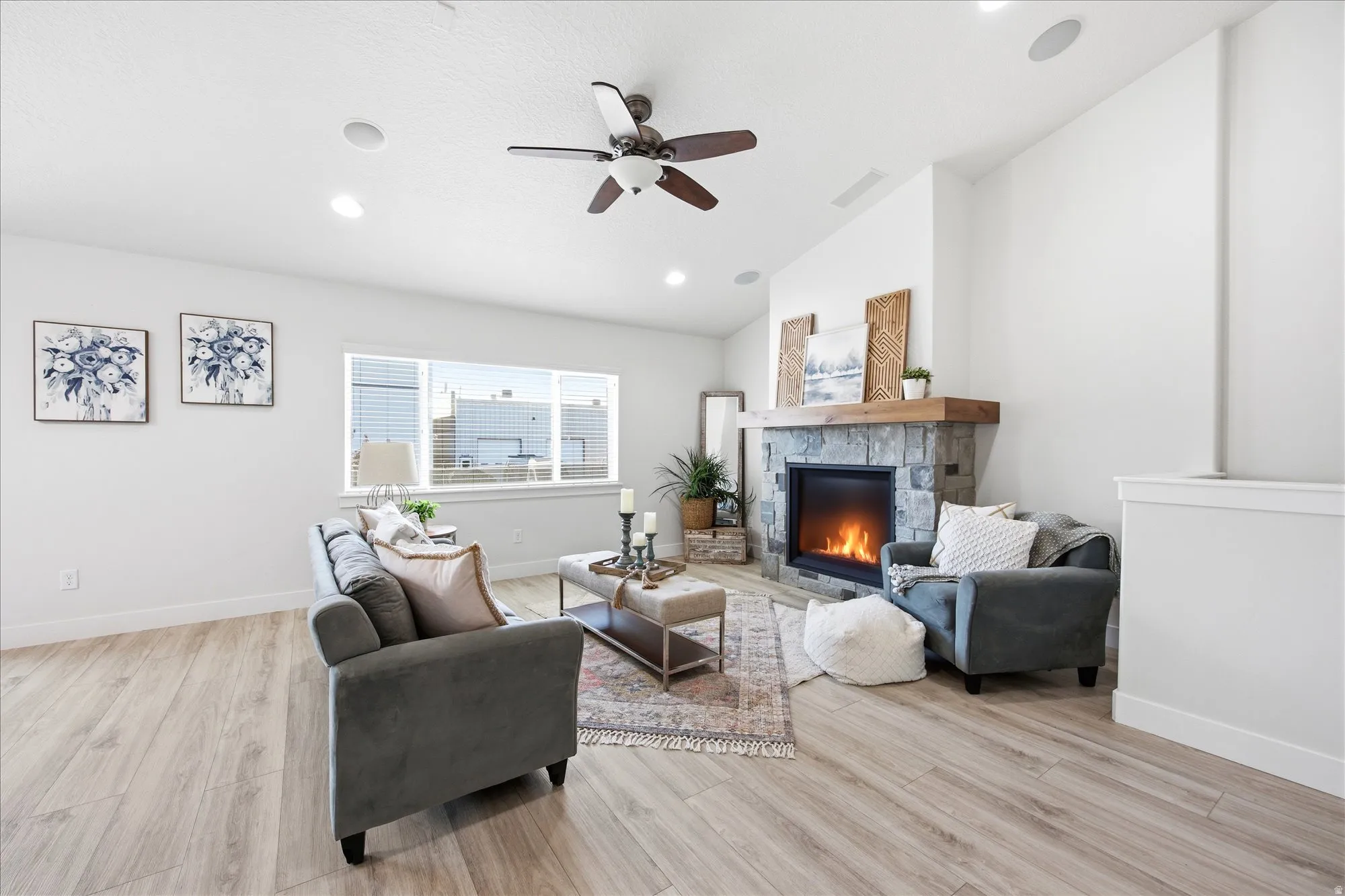Bright living space featuring a stone fireplace with a wood-beam mantel, wood-finish flooring, and recessed lighting