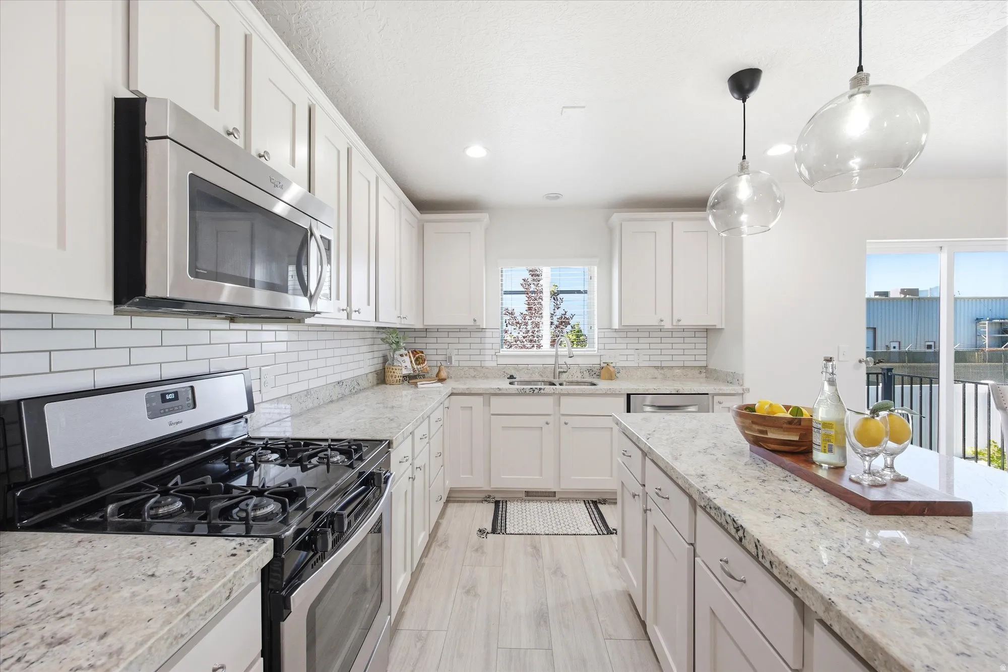 Bright kitchen featuring white shaker cabinetry, stainless steel appliances, light granite countertops, white subway tile backsplash, and light wood-finish flooring