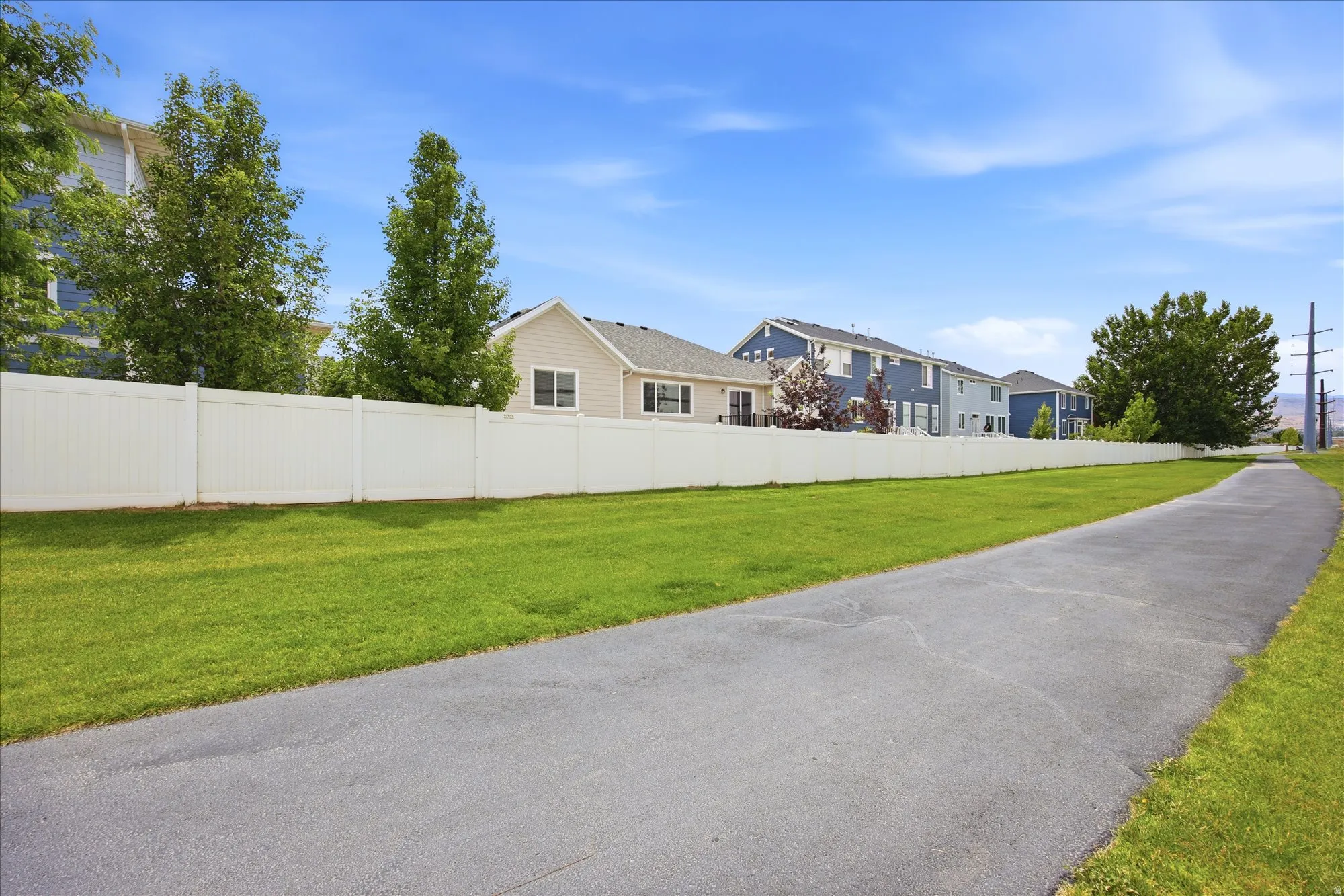 Paved pathway bordered by manicured green space and a privacy fence