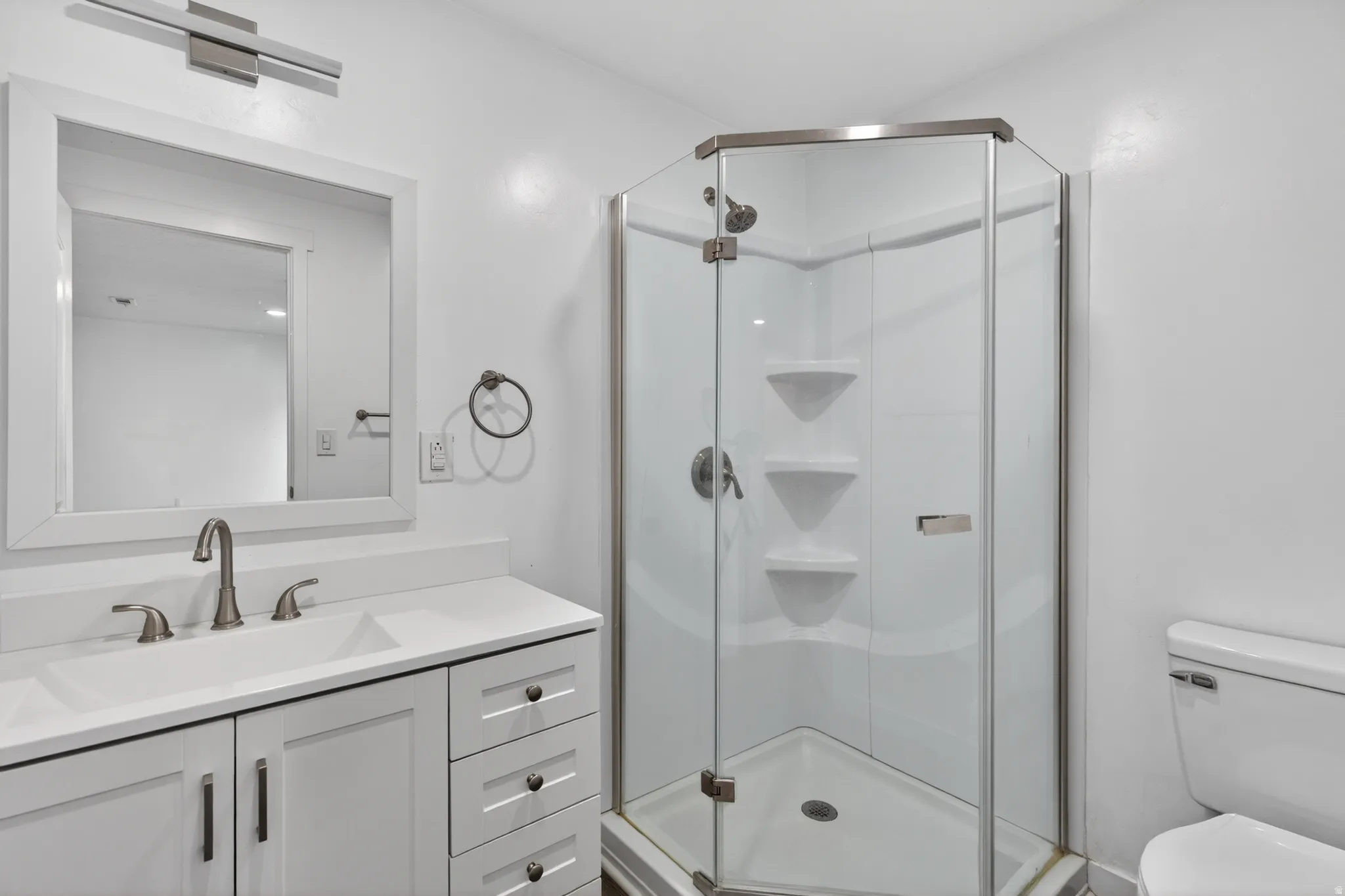 Bathroom with a corner glass-enclosed shower, white vanity with an integrated sink, and brushed nickel fixtures