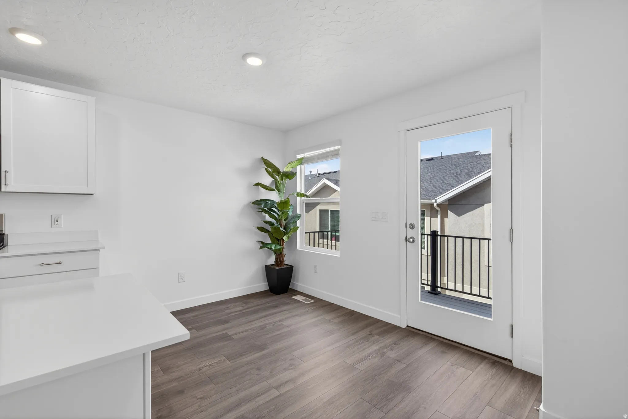 Bright interior space featuring wood-finish flooring, recessed lighting, and a white framed glass door leading to an outdoor balcony with black railings