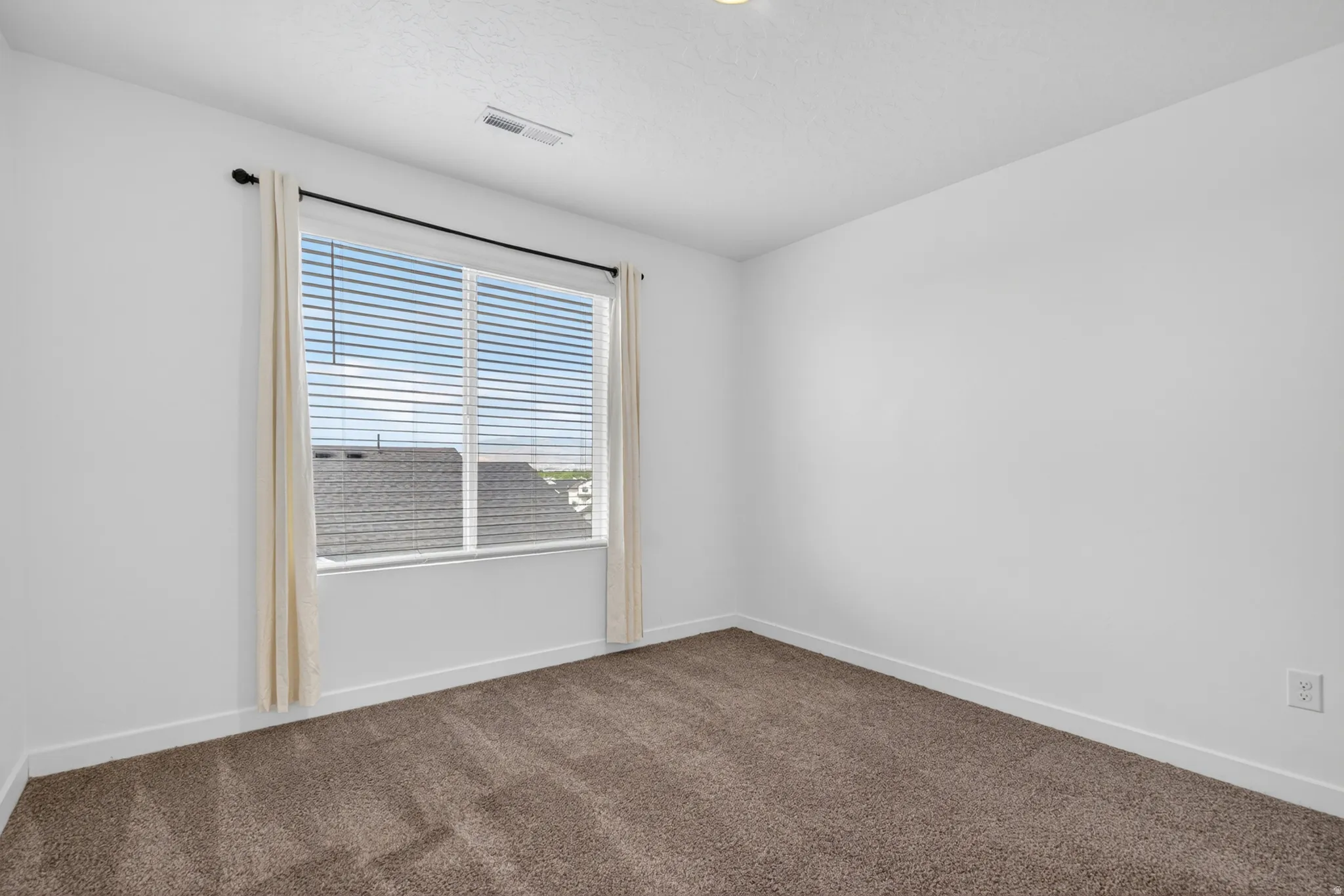 Spacious room featuring neutral carpeting, white walls, a large window with blinds, and recessed lighting