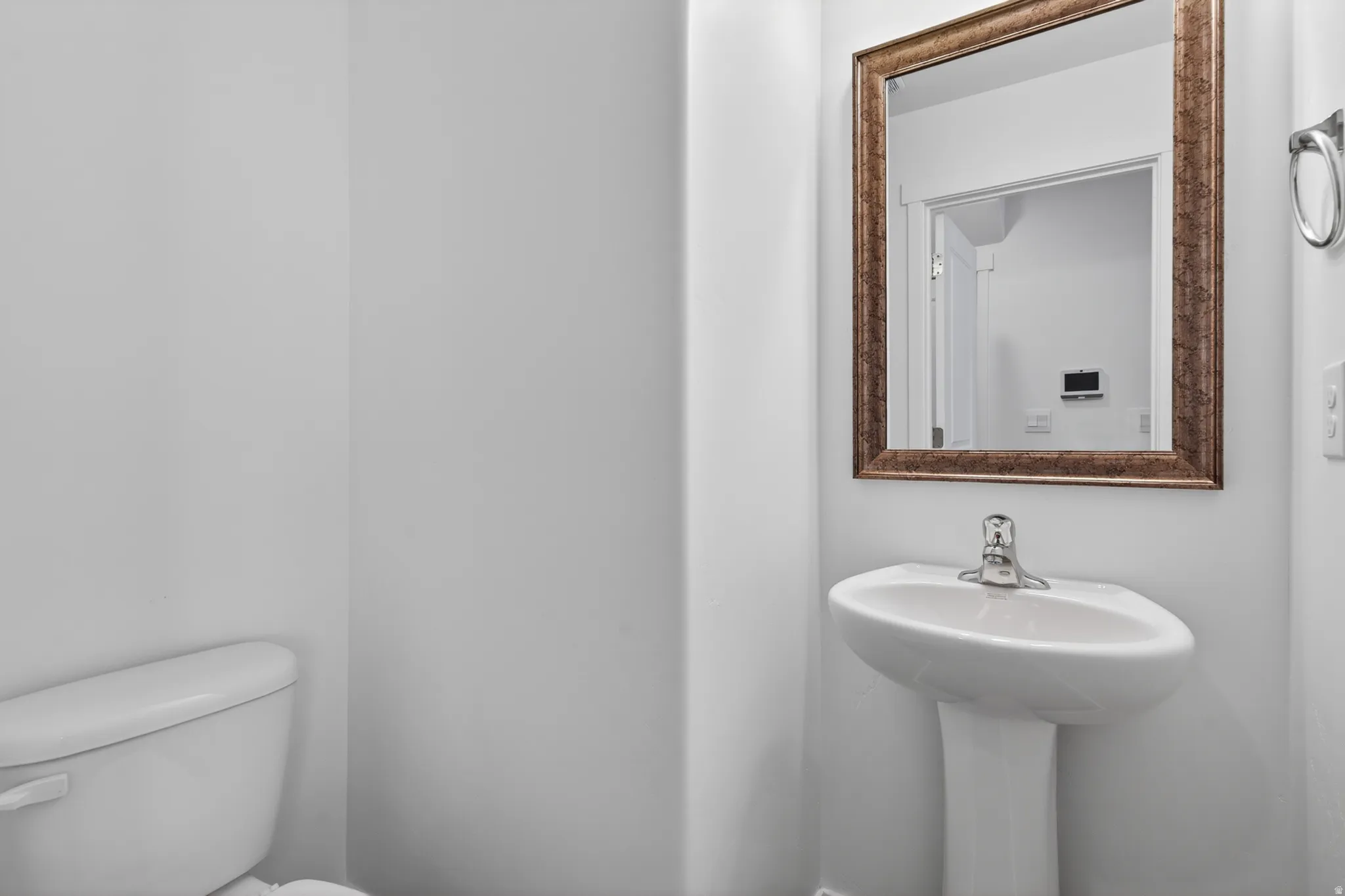 White pedestal sink with a single-handle chrome faucet and an ornate framed mirror