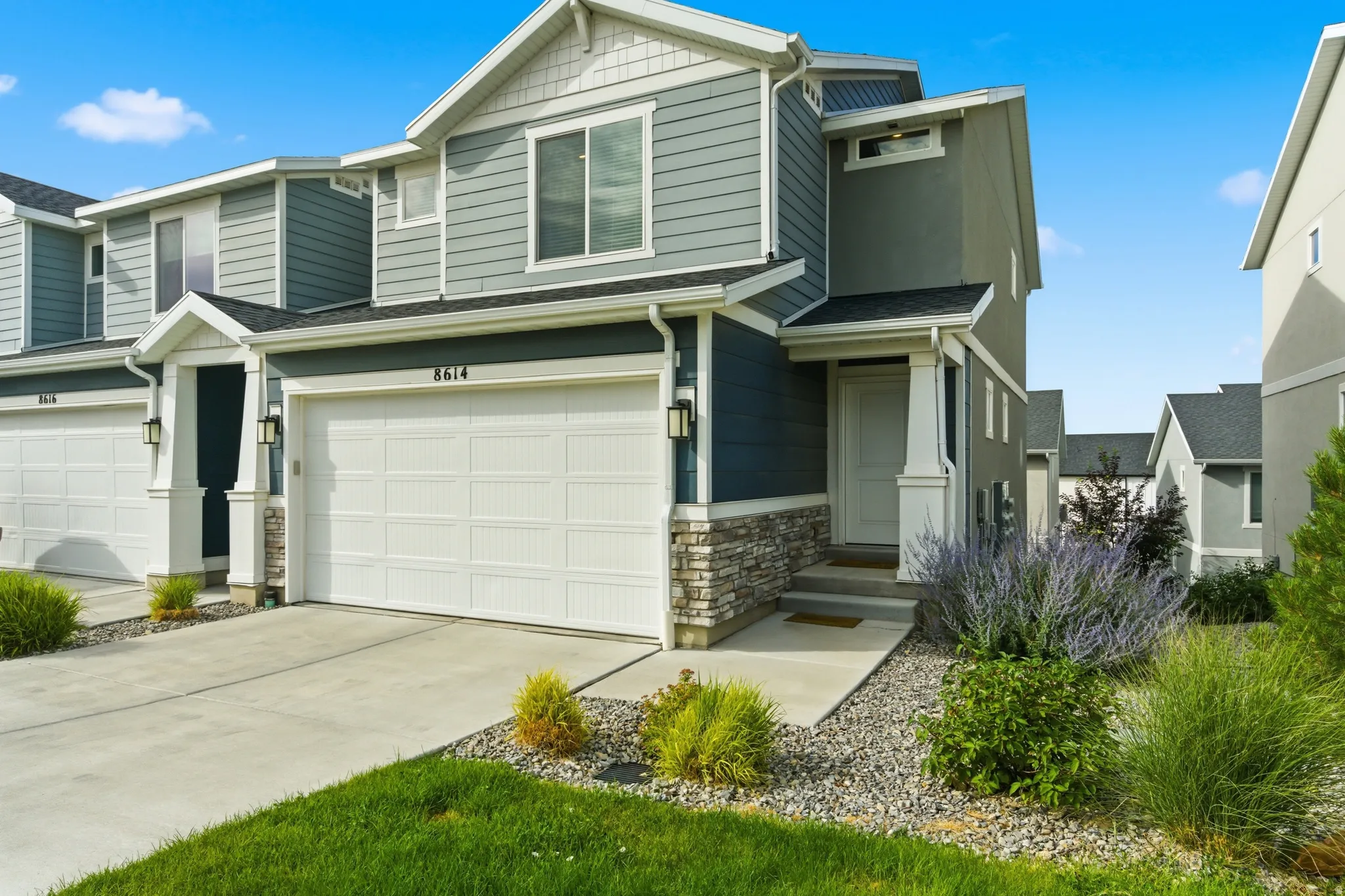 Modern multi-story exterior with a covered entry, stone accent detailing, a two-car garage, and established landscaping