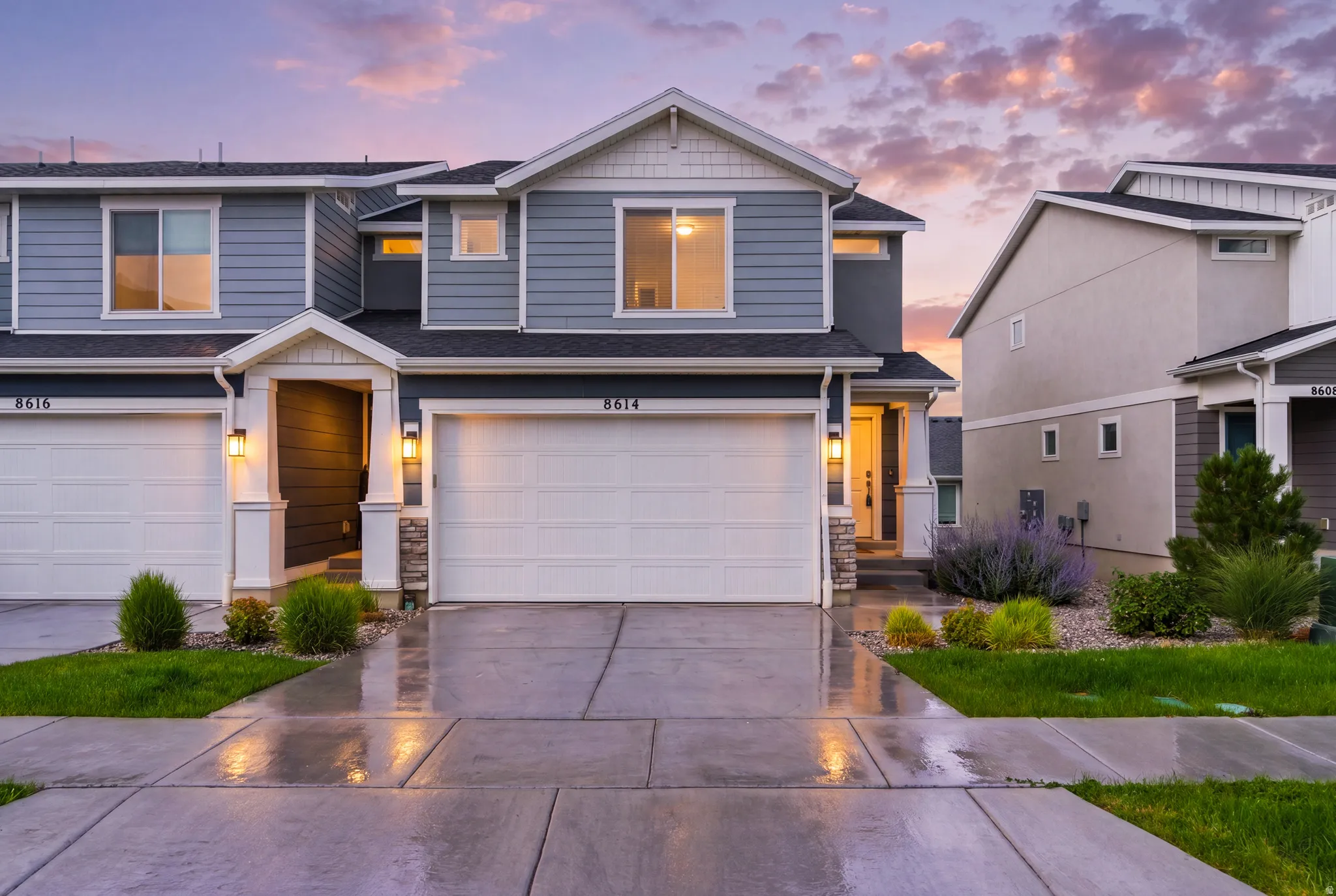 Modern exterior featuring blue siding with white trim, a covered entryway with stone accents, an attached two-car garage, and a concrete driveway