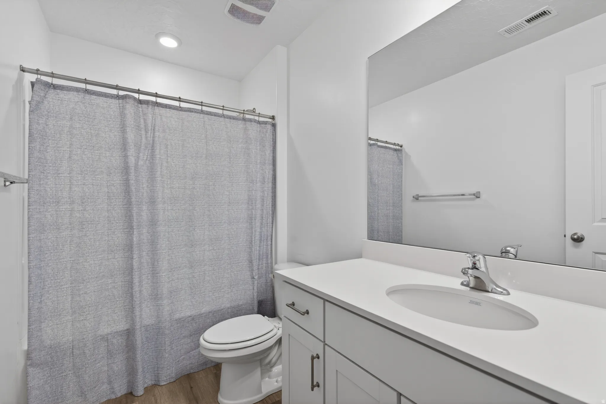 Bathroom featuring a single vanity with an undermount sink, a large wall-mounted mirror, a toilet, a shower/tub combination, and wood-finish flooring