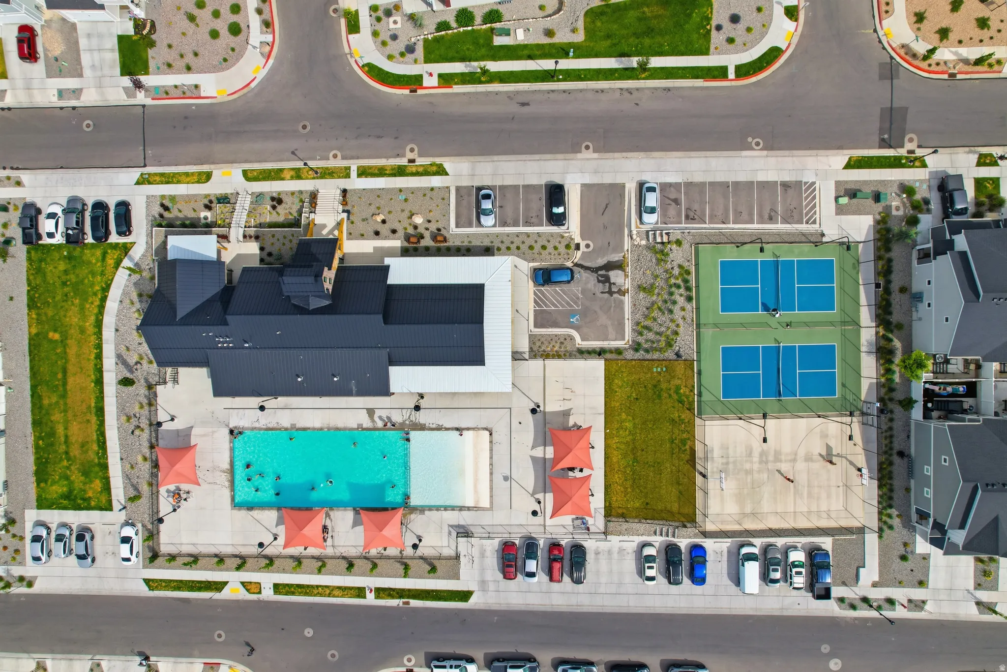 Community recreation area featuring a swimming pool, two pickleball courts, a basketball court, and a club house with a black roof