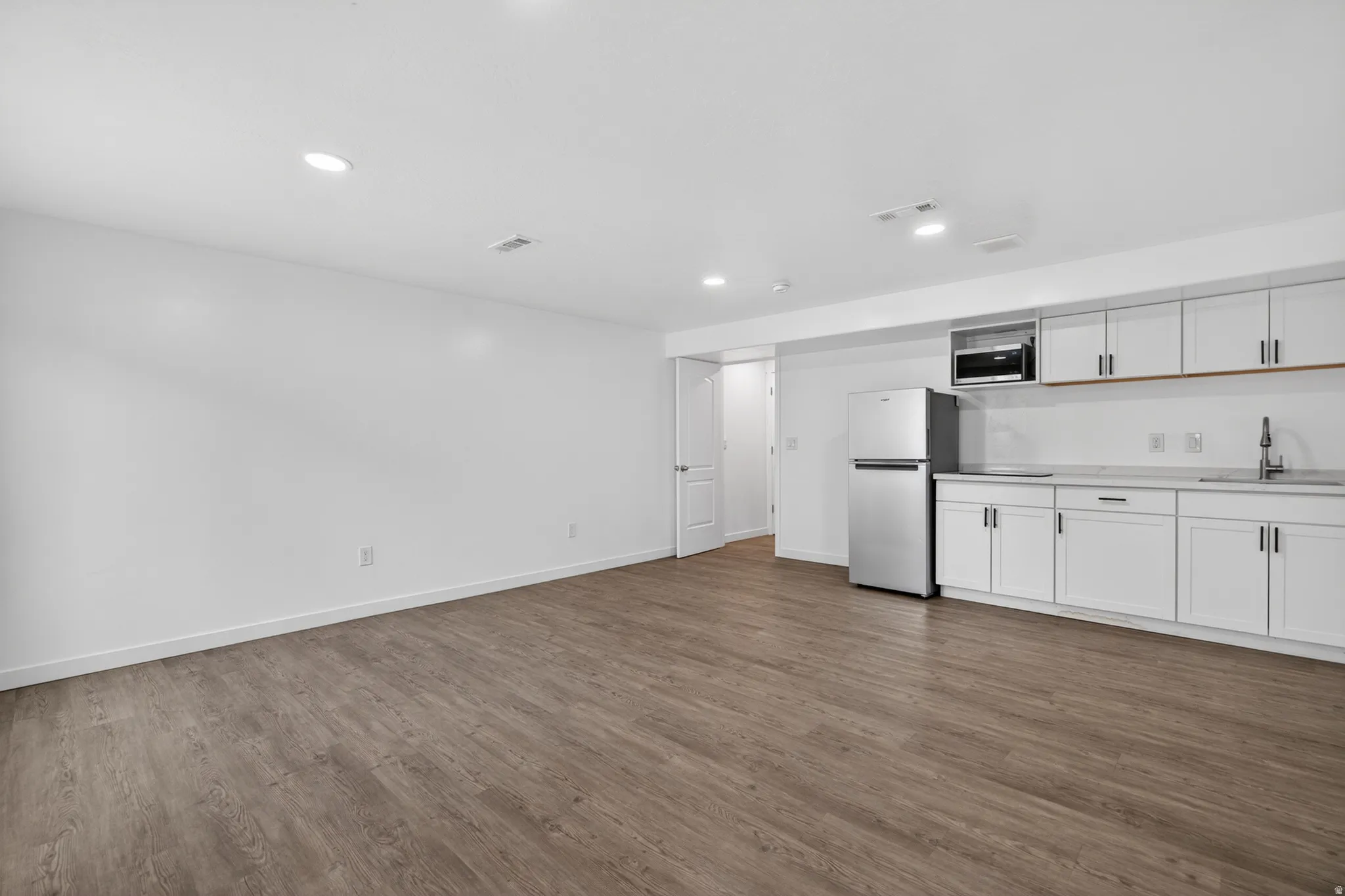 Open concept living area featuring wood-finish flooring, recessed lighting, and a kitchen area with white cabinetry, a stainless steel refrigerator, and a built-in microwave