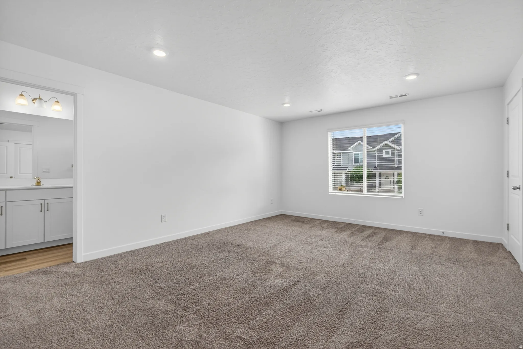 Spacious room featuring neutral carpeting, white walls, recessed lighting, and a large window with horizontal blinds
