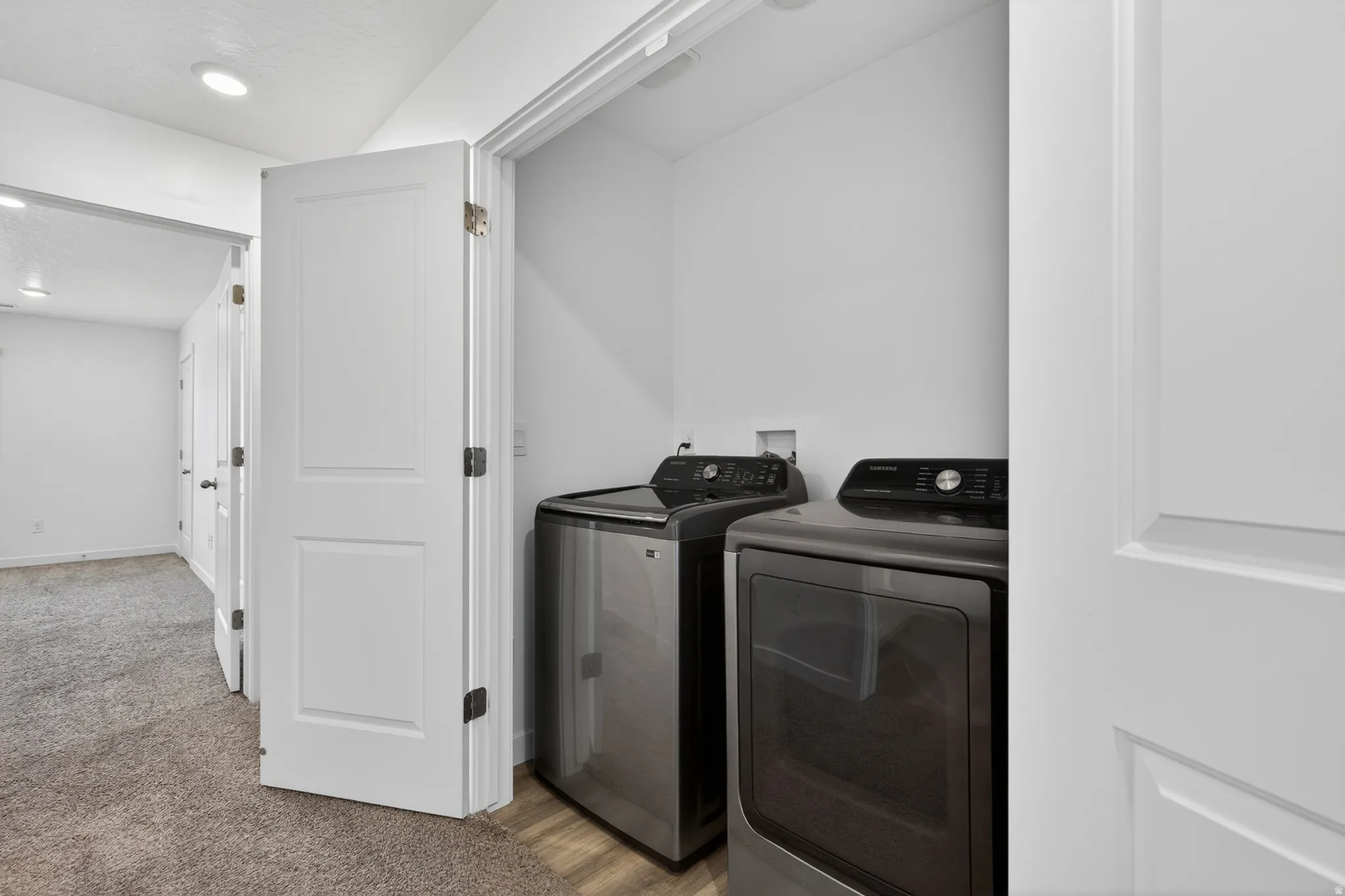 Dedicated laundry closet featuring modern appliances, wood-finish flooring, and bright white walls