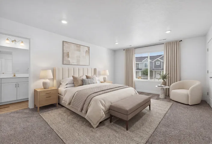 Spacious room featuring neutral carpeting, recessed lighting, a large window with blinds, and an entryway to an adjacent bathroom with a light wood-finish vanity and wall-mounted lighting