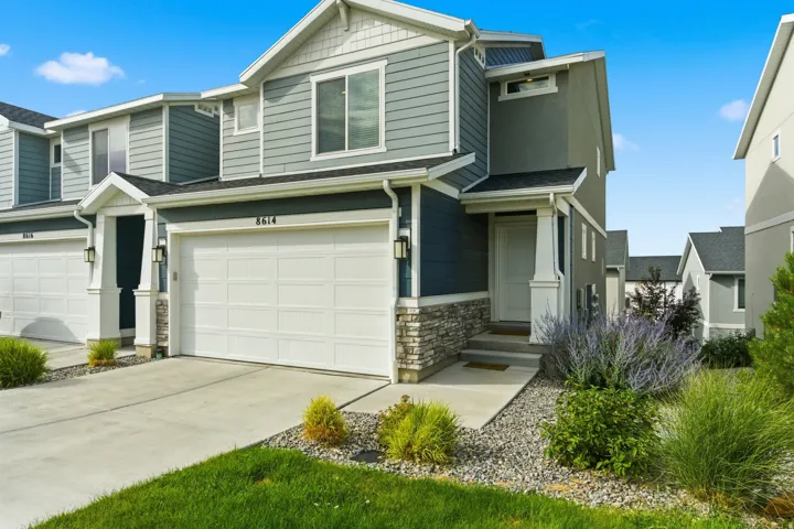 Modern multi-story exterior with a covered entry, stone accent detailing, a two-car garage, and established landscaping