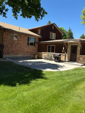 Expansive backyard featuring a lush lawn, a concrete patio, brick and wood-paneled exterior, a stone-clad entry, and multiple exterior windows