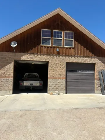 Two-story structure featuring a stone and brick veneer lower level with two garage doors, and a wood-paneled upper level with three windows