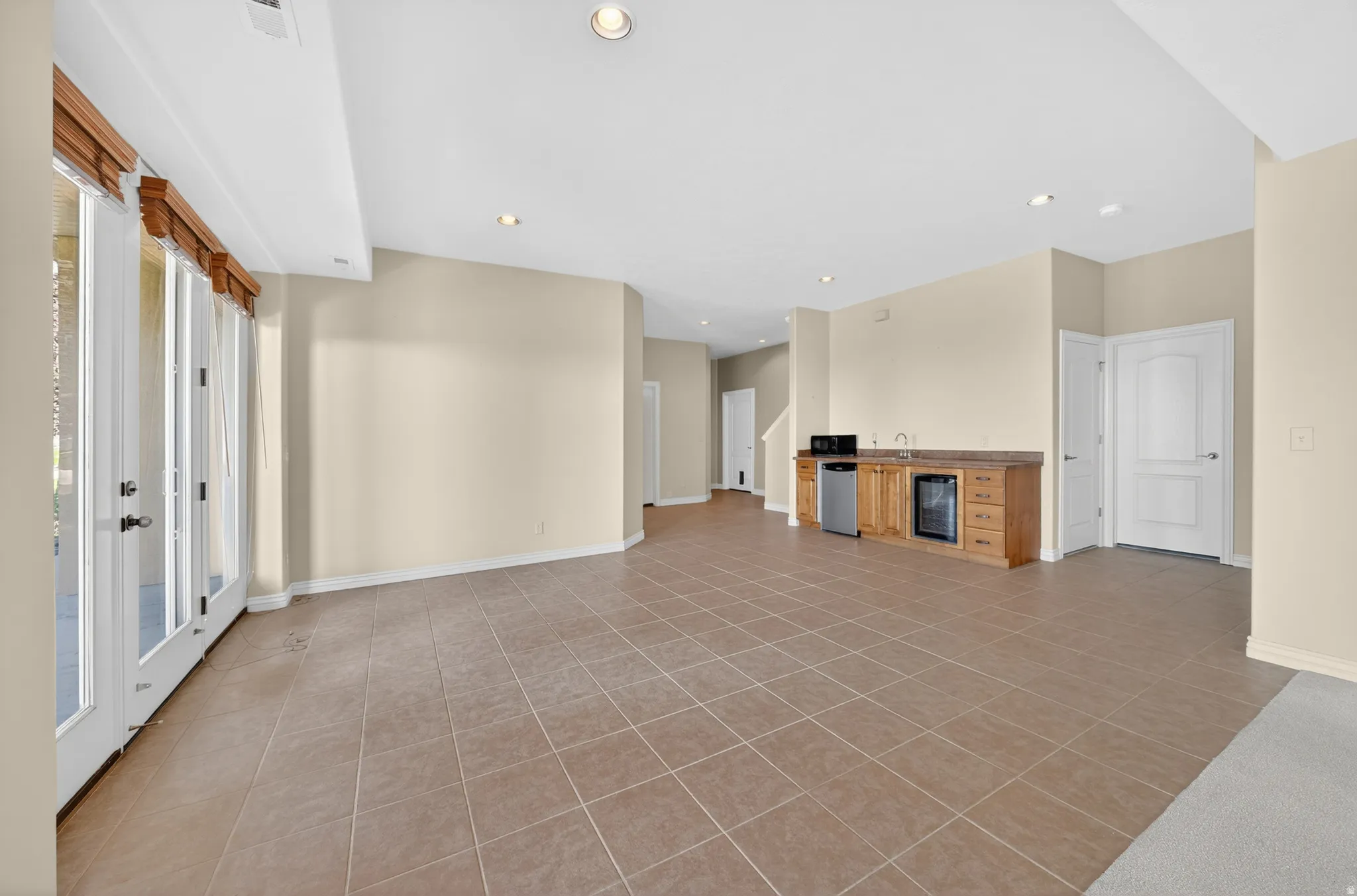 Spacious lower-level area with tile flooring, a built-in wet bar featuring a beverage cooler and microwave, and recessed lighting