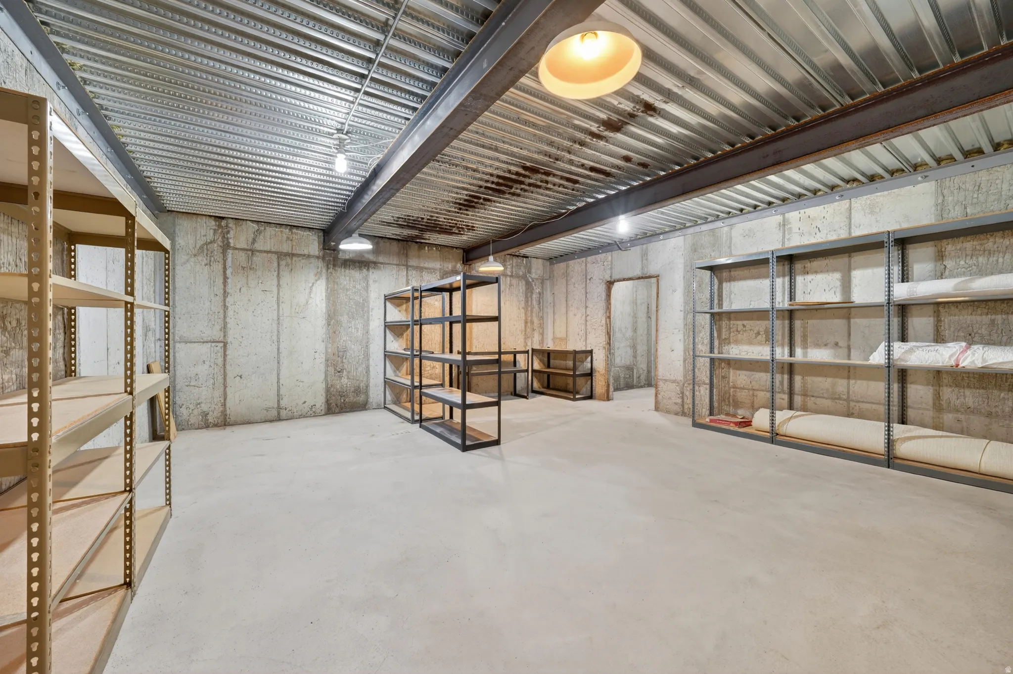 Spacious basement  storage room featuring concrete walls, a concrete floor, and exposed metal beam ceiling