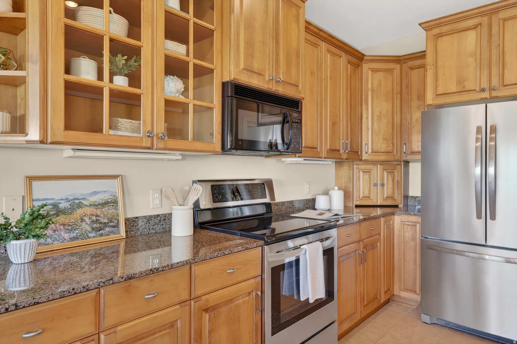 Kitchen featuring light wood cabinetry with crown molding, glass-front upper cabinets, stainless steel appliances, and granite countertops