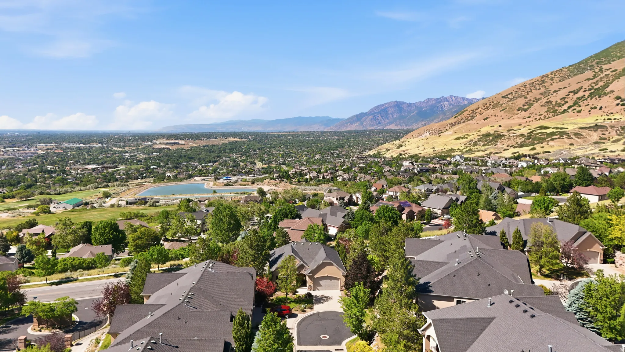 Aerial perspective showcasing a residential area with varied rooflines and abundant mature trees, set against a backdrop of mountains and valley