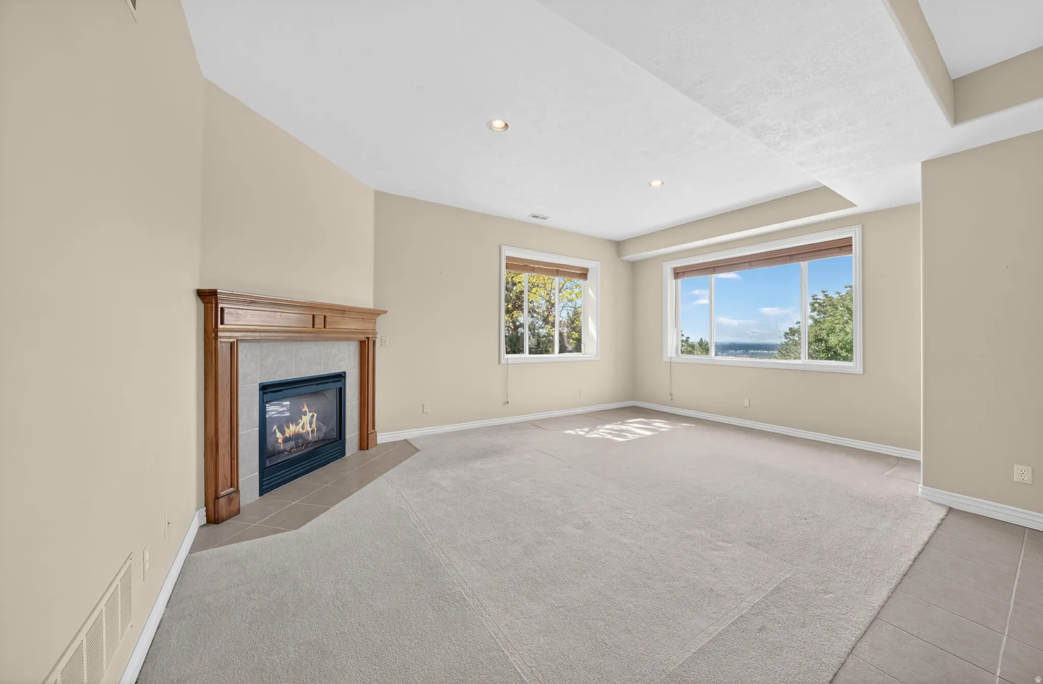 Spacious room featuring a fireplace with a wood mantle and tile surround, two large windows, recessed lighting, and carpeted flooring