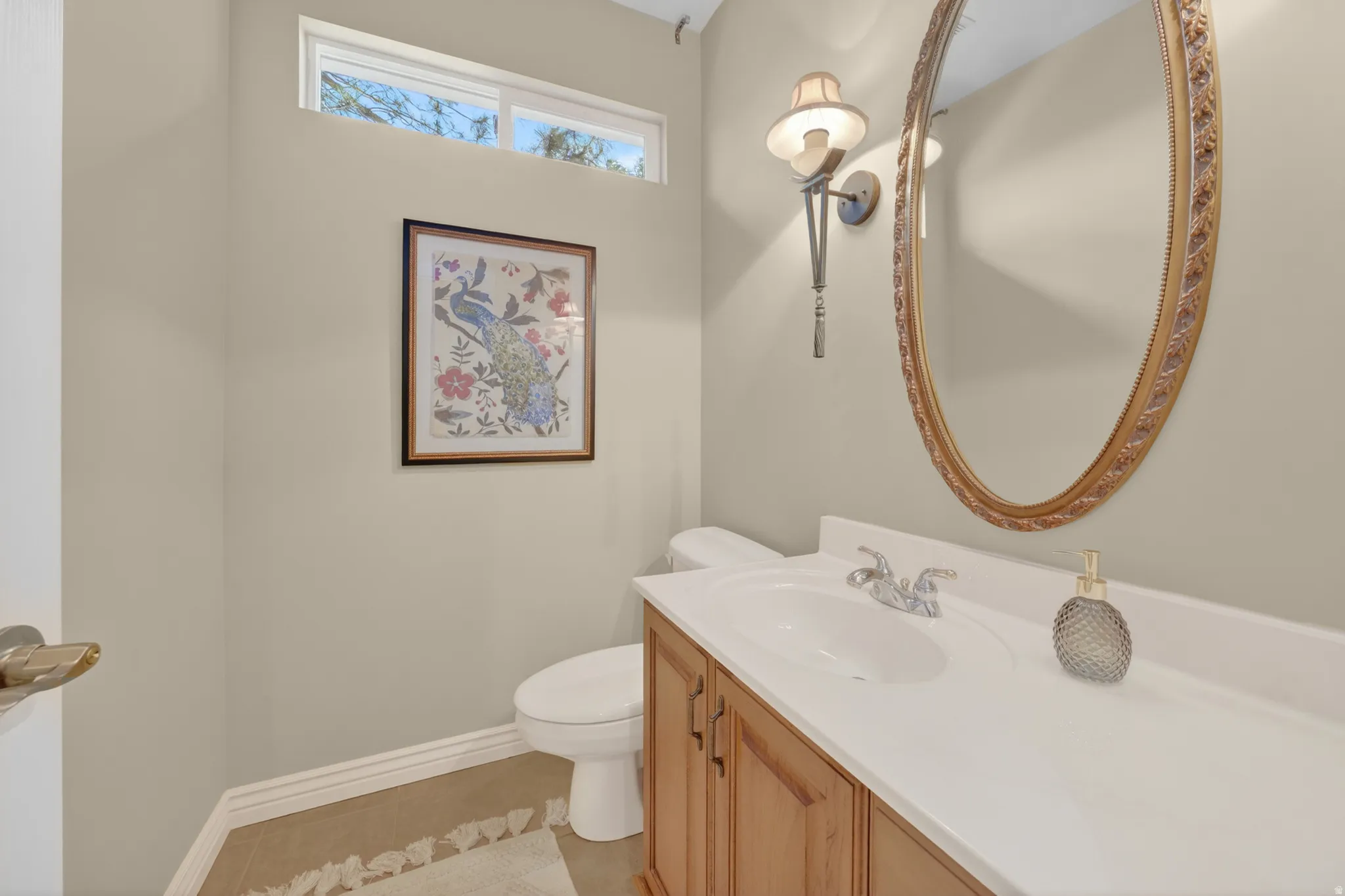 Guest Bathroom featuring a wood-finish vanity with a white countertop and integrated sink, chrome faucet, and an ornate oval mirror